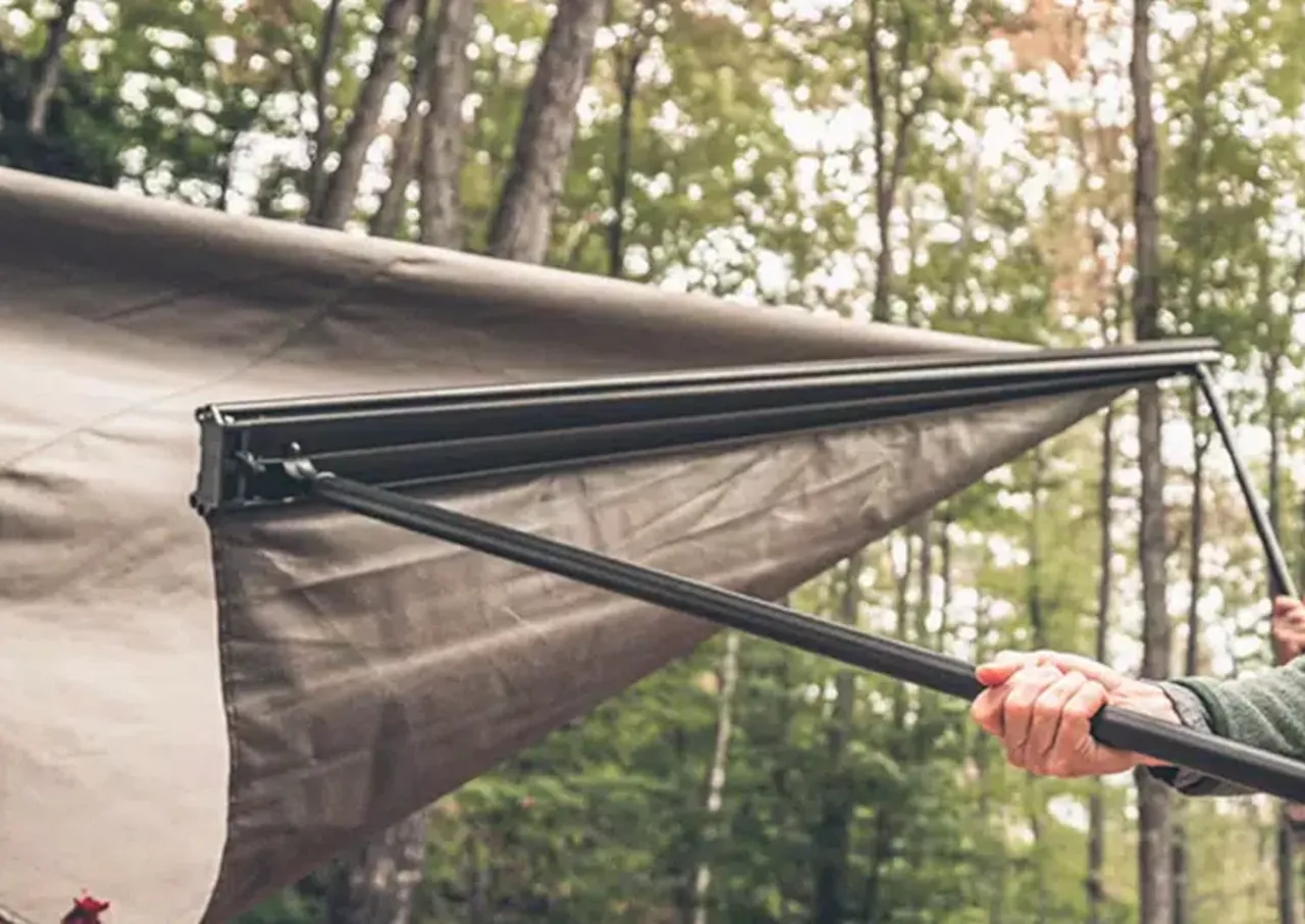 Person setting up a tent in a wooded area.