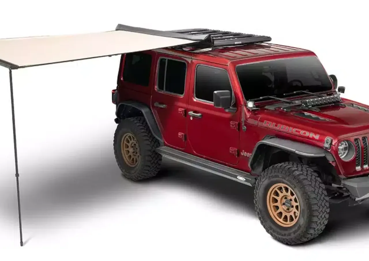 Red Jeep Wrangler with a rooftop tent and an attached canopy for shade.