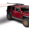 Red Jeep Wrangler with a rooftop tent and an attached canopy for shade.