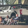 People relaxing under a truck-turned-campsite with a dog nearby during outdoor camping.
