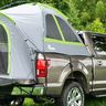 Pickup truck with a pop-up tent attached in a grassy, wooded area.