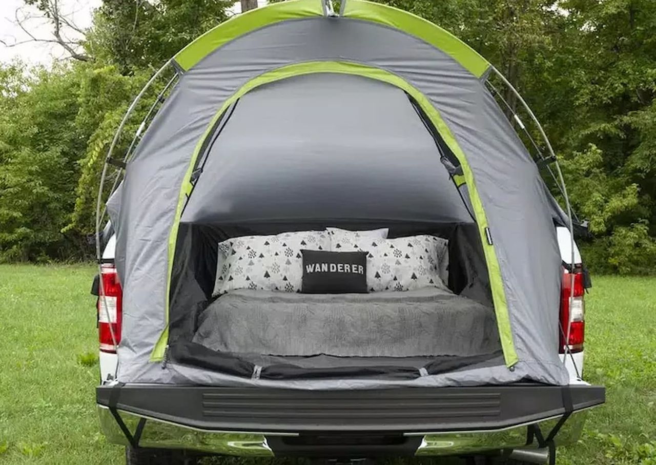 Tent set up in the back of a truck with bedding and pillows inside, outdoors.