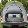 Tent set up in the back of a truck with bedding and pillows inside, outdoors.