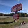 A roadside sign for "Pasties" with additional signs for "Lehto's," "Smoked Fish," and "Beef Jerky" on a grassy area under a blue sky.