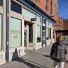 Person in a winter coat walking past Duluth Coffee Company, a cafe with large windows on a sunny street.