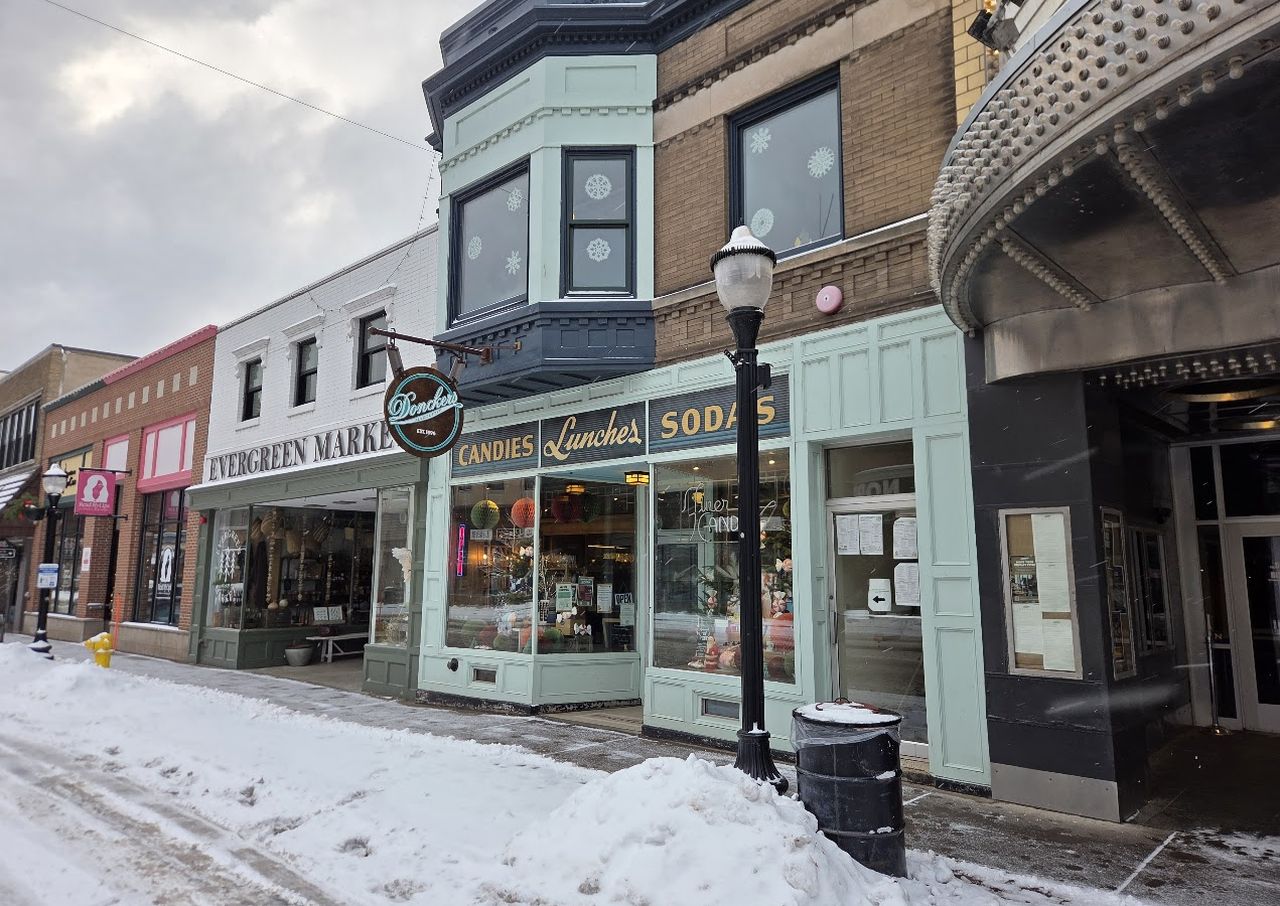 Snowy street with vintage storefronts, including Donckers diner. Overcast sky and snow-covered sidewalk and road.