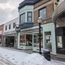 Snowy street with vintage storefronts, including Donckers diner. Overcast sky and snow-covered sidewalk and road.