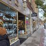 Woman in a brown hat walking past a storefront with holiday decorations and a sign reading "Come shop for you and your honey."
