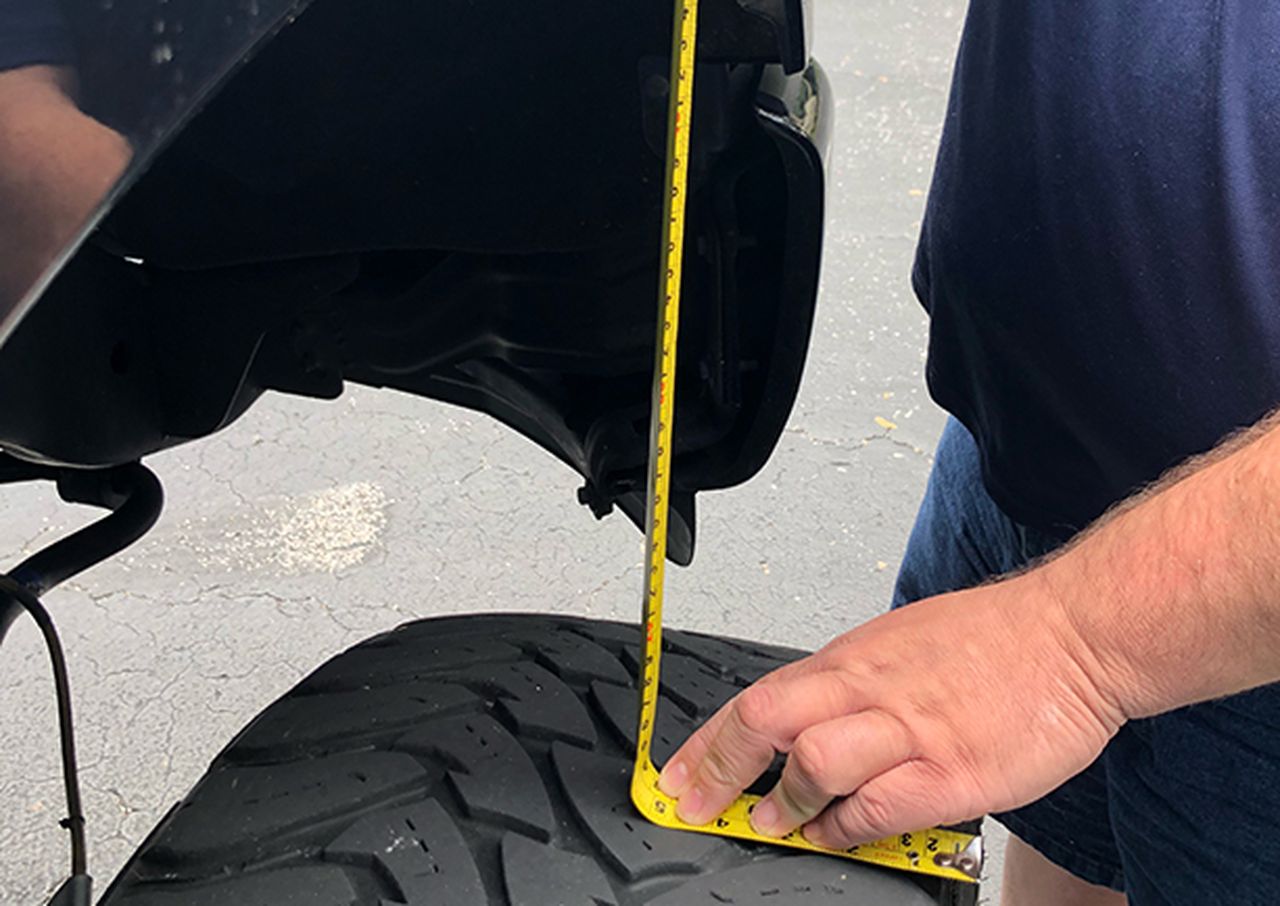Person measuring a vehicle tire with a yellow tape measure.