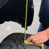 Person measuring a vehicle tire with a yellow tape measure.