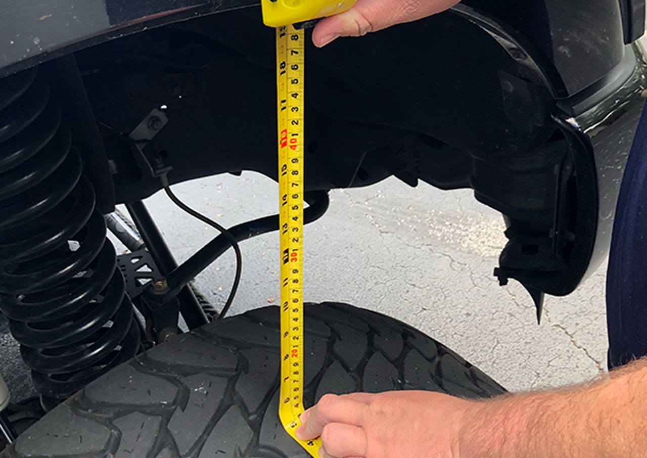 Measuring tire tread depth with a tape measure on a vehicle.