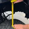 Measuring tire tread depth with a tape measure on a vehicle.